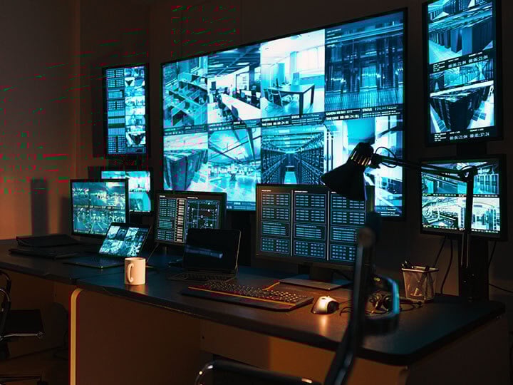 Business security command center showing security camera feeds and laptops with controls on the desk